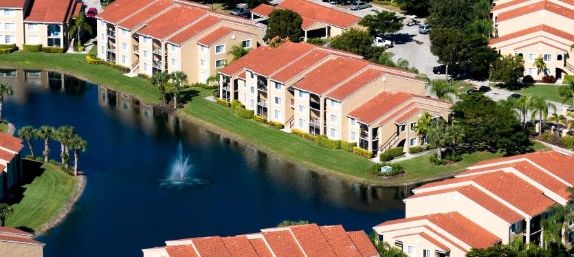 Imagen aérea de un barrio que incluye un estanque y una fuente, con casas y áreas verdes alrededo