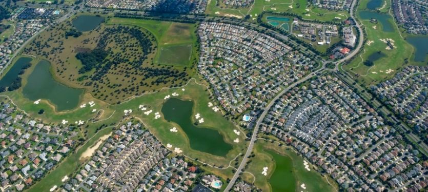 Imagen aérea de un vecindario suburbano, con casas y árboles, cerca de una gran ciudad.