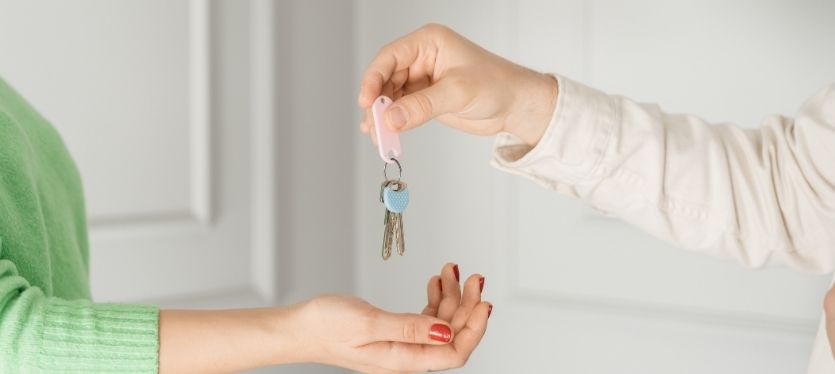 A woman is giving a key to another individual, indicating a change in ownership or access