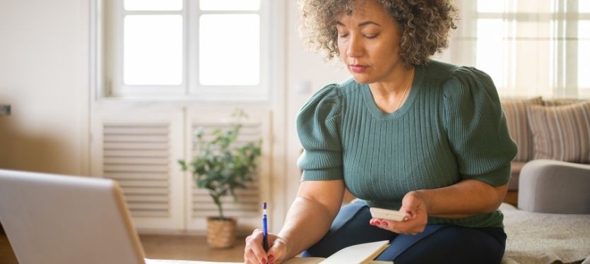 Mujer sentada en el suelo, trabajando en un portátil y sosteniendo un bolígrafo, inmersa en su actividad