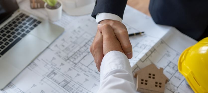 Dos individuos se dan la mano en un sitio de construcción, representando un acuerdo en un proyecto