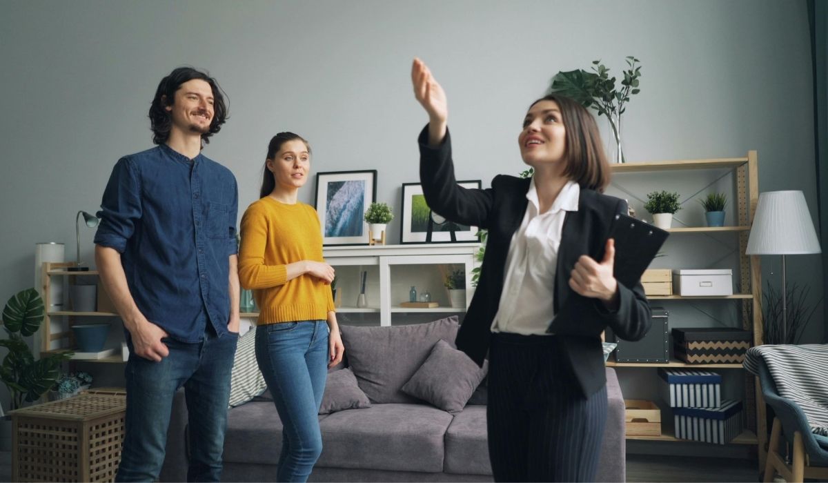 Una agente inmobiliaria enseña a un hombre y dos mujeres la tendencia en florida que es una sala de estar acogedora