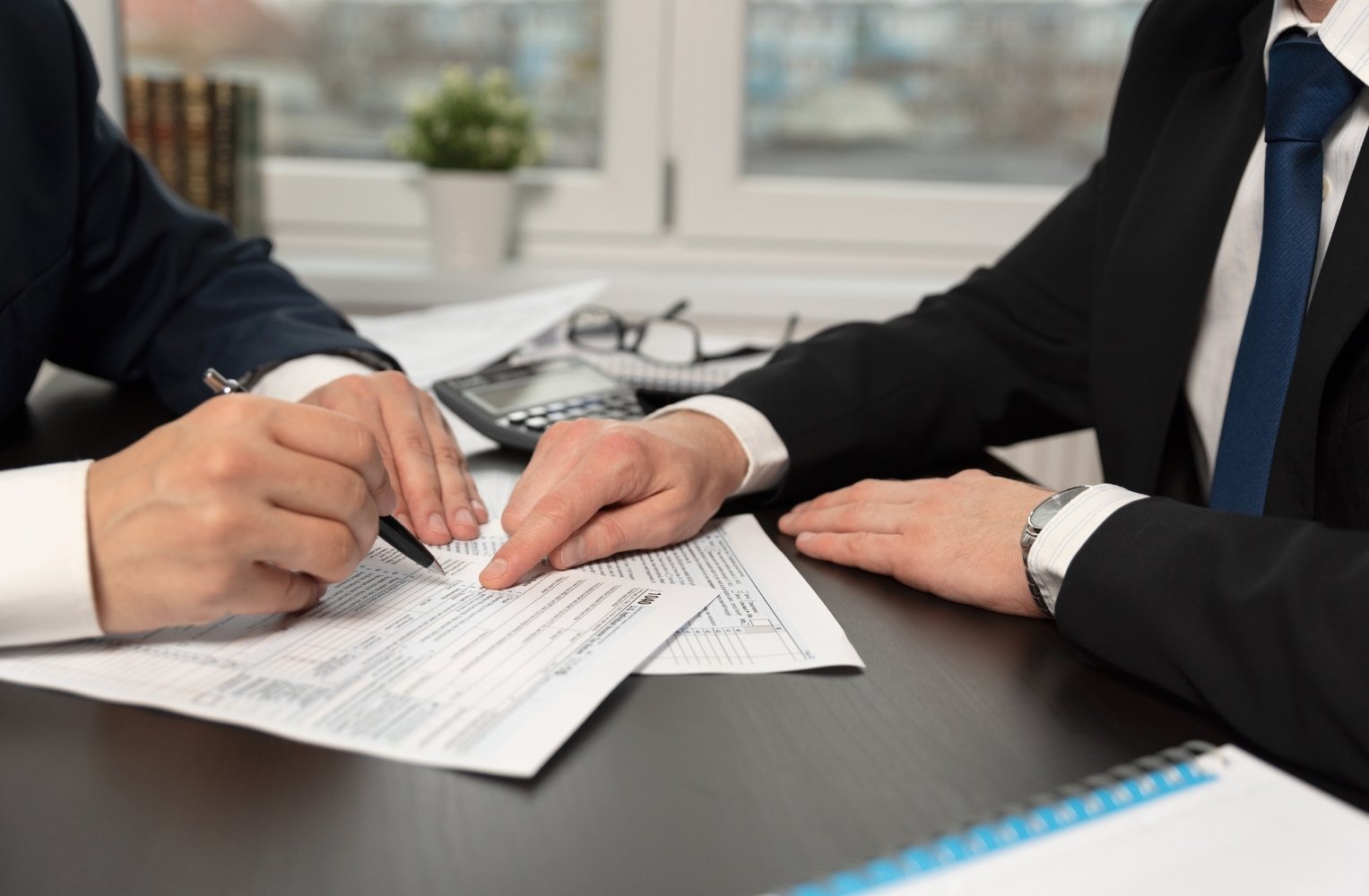 Dos personas de negocios firman documentos en un escritorio, discutiendo sobre FIRPTA y su impacto en la inversión.