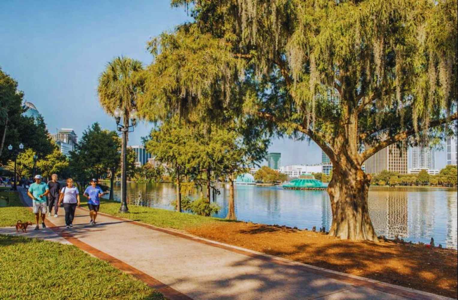 Personas caminando por un sendero junto a un lago, rodeados de árboles y edificios en Winter Garden, Orlando.