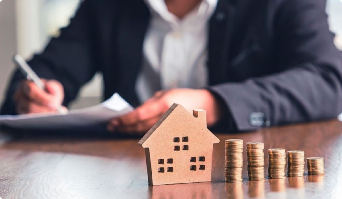 Hombre en traje sentado en un escritorio con monedas y un modelo de casa, ilustrando una guía de inversión en Florida.