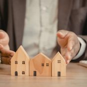 Un hombre sostiene un modelo de casa de madera sobre una mesa.