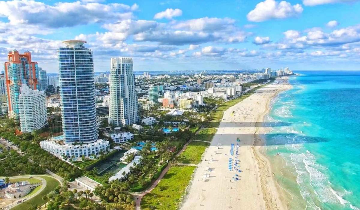 Playa de Miami Beach, Florida, con arena blanca y aguas turquesas bajo un cielo soleado.