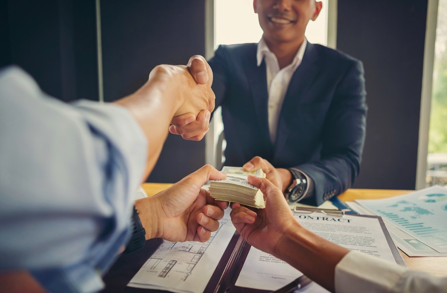 Personas de negocios estrechando manos sobre una mesa con dinero.