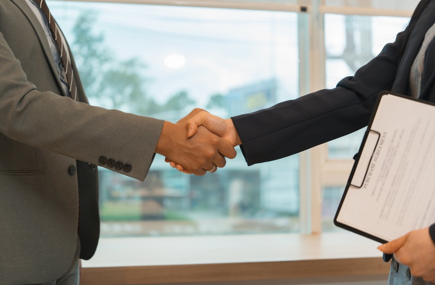 Dos profesionales de negocios estrechando manos sobre un portapapeles.