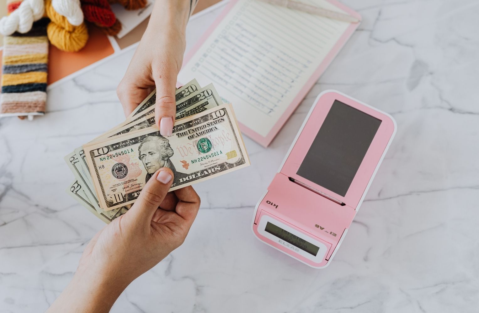 Persona sosteniendo dinero frente a una caja registradora rosa.