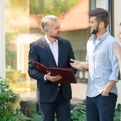 Un agente inmobiliario profesional asesorando a una pareja joven frente a una propiedad.