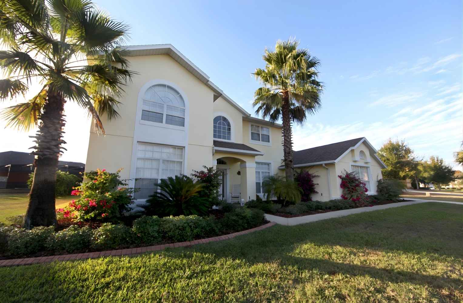 Fachada de una casa residencial de dos niveles en Florida con palmeras y jardín frontal.