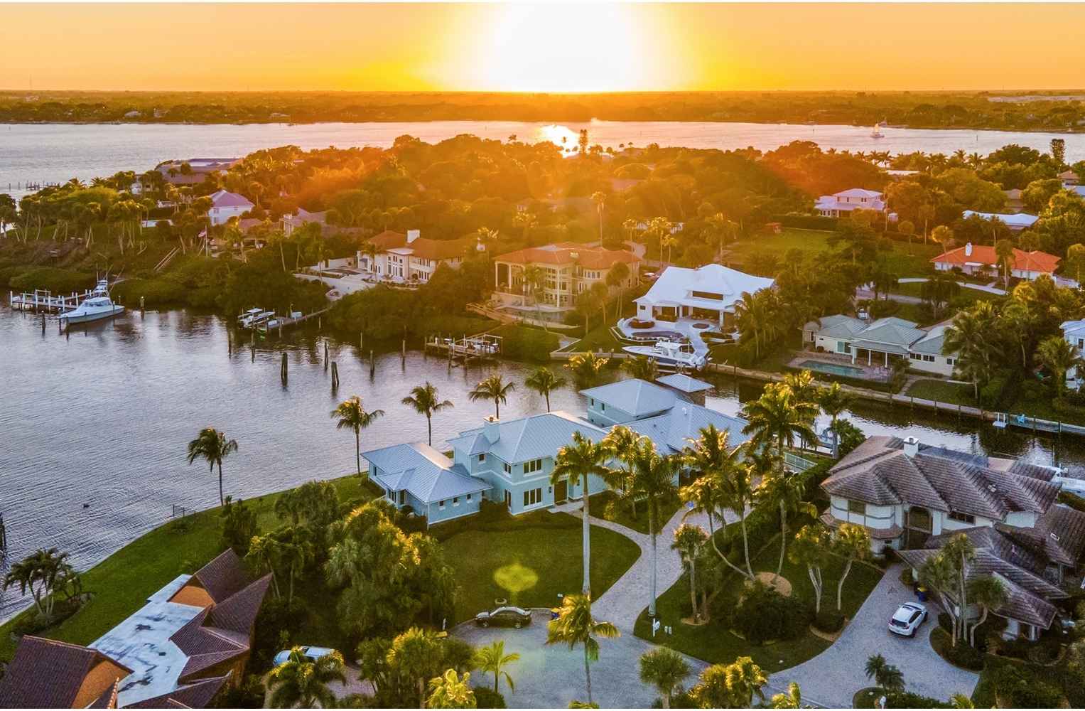 Atardecer dorado sobre mansiones de lujo con embarcaderos privados en una zona costera de Florida.