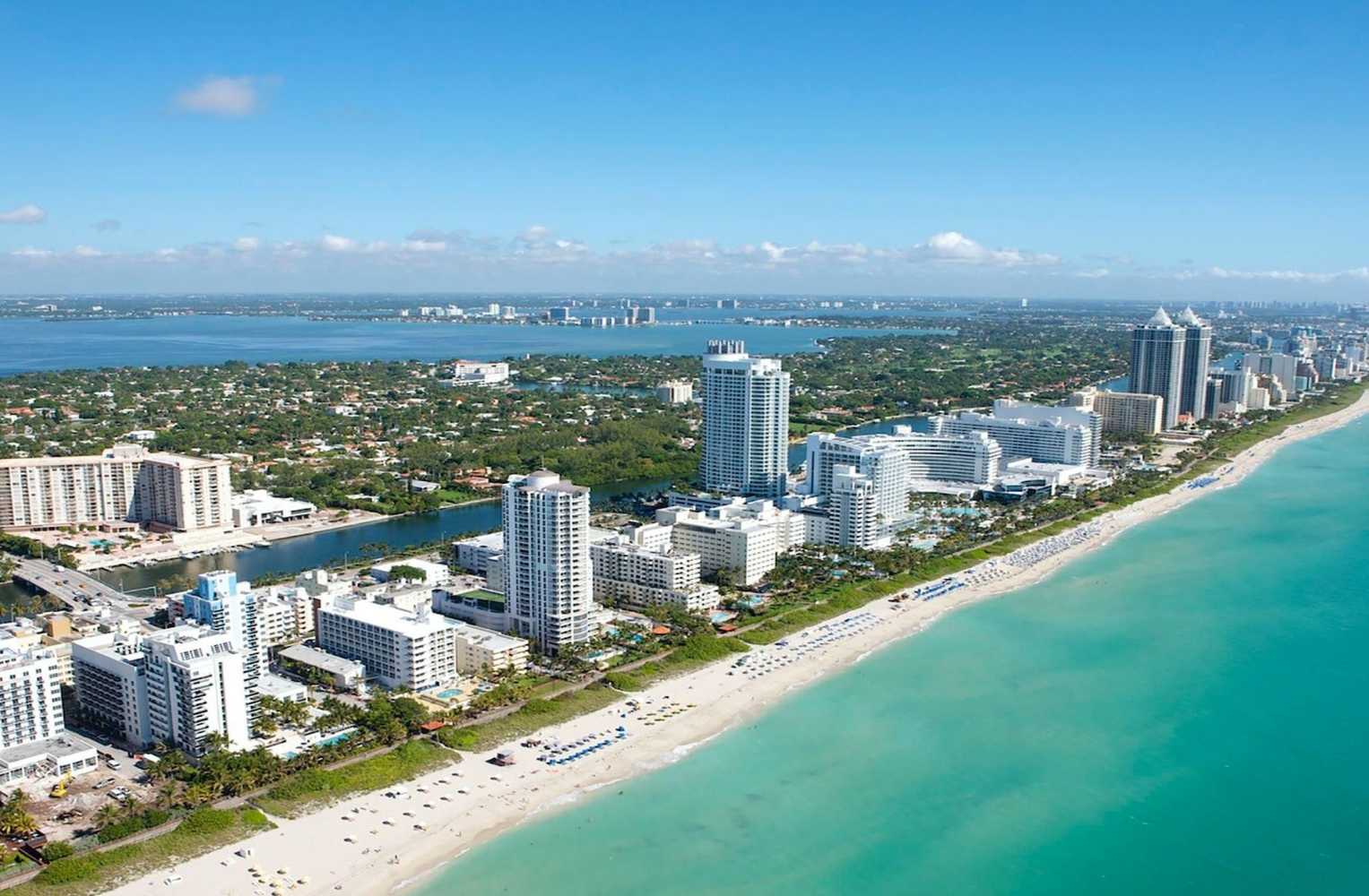 Vista aérea de la costa de Florida con edificios modernos, playas de arena blanca y aguas turquesas.