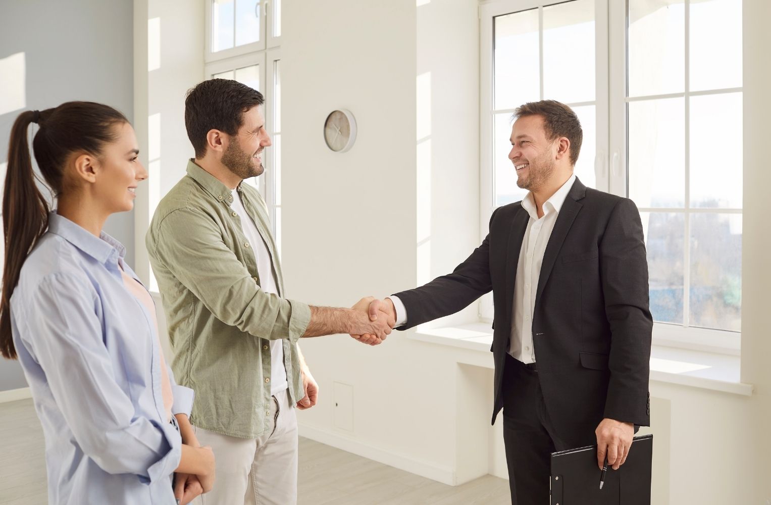 A real estate agent shaking hands with a young couple in a bright apartment, representing success in property purchases and foreign investment in Doral, Florida.