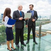 Tres profesionales de negocios vestidos de traje conversando en la terraza de un edificio corporativo.