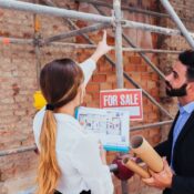 Agente inmobiliario y cliente revisando planos de una propiedad en preventa frente a una obra en construcción con andamios en Florida.