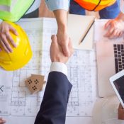 Cierre de contrato inmobiliario mediante un apretón de manos sobre planos de arquitectura.