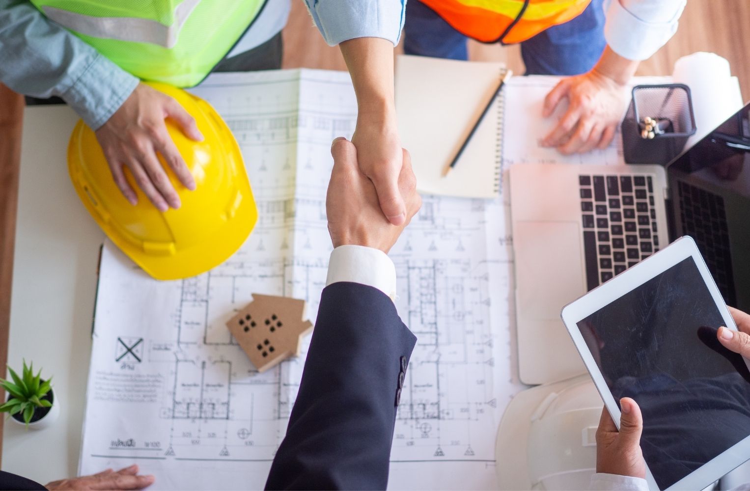 Cierre de contrato inmobiliario mediante un apretón de manos sobre planos de arquitectura.