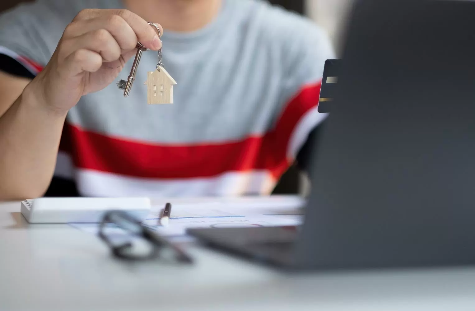 A real estate investor holding house keys in front of a laptop.