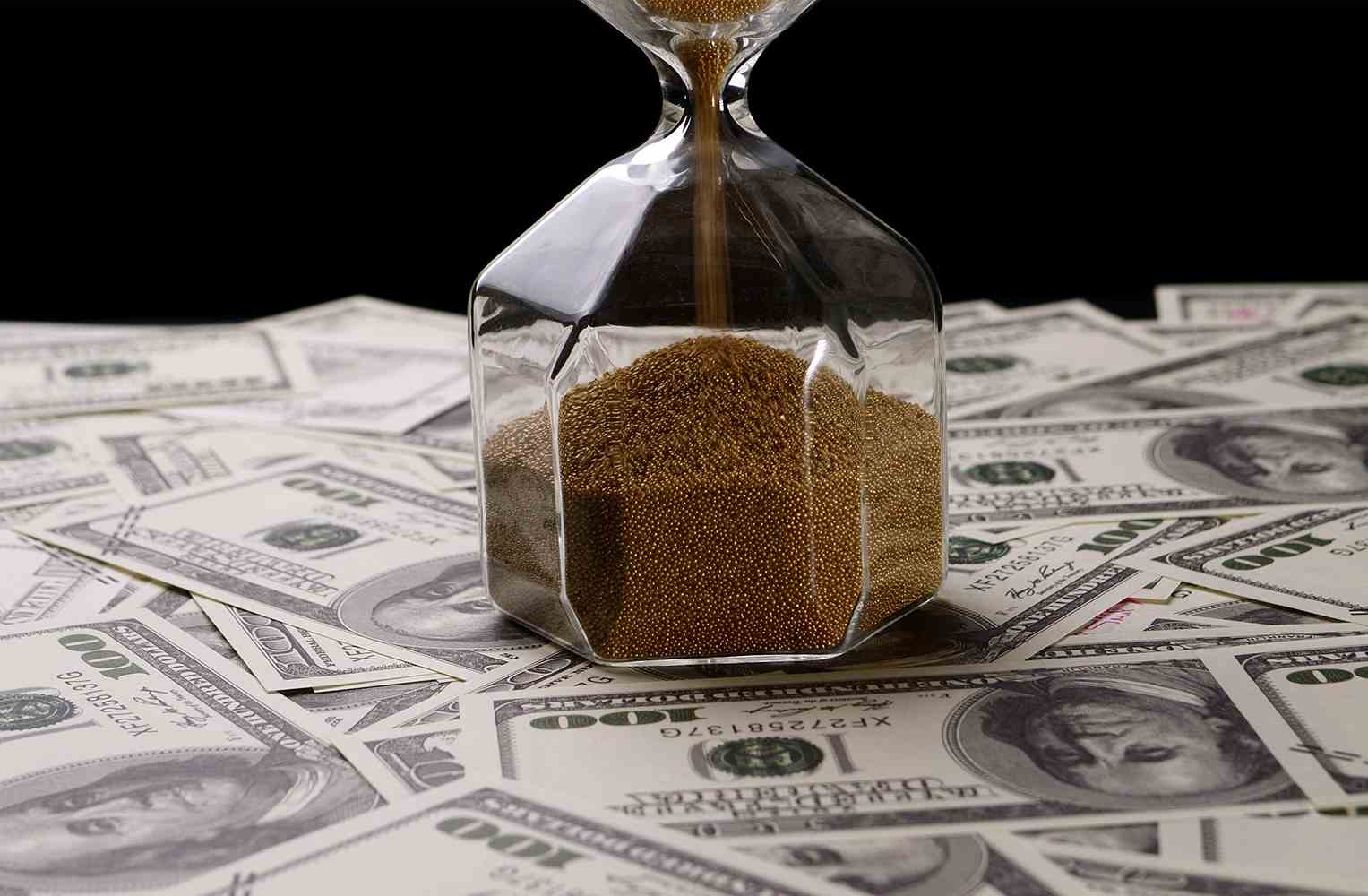 Reloj de arena con arena dorada sobre una cama de billetes de 100 dólares americanos.