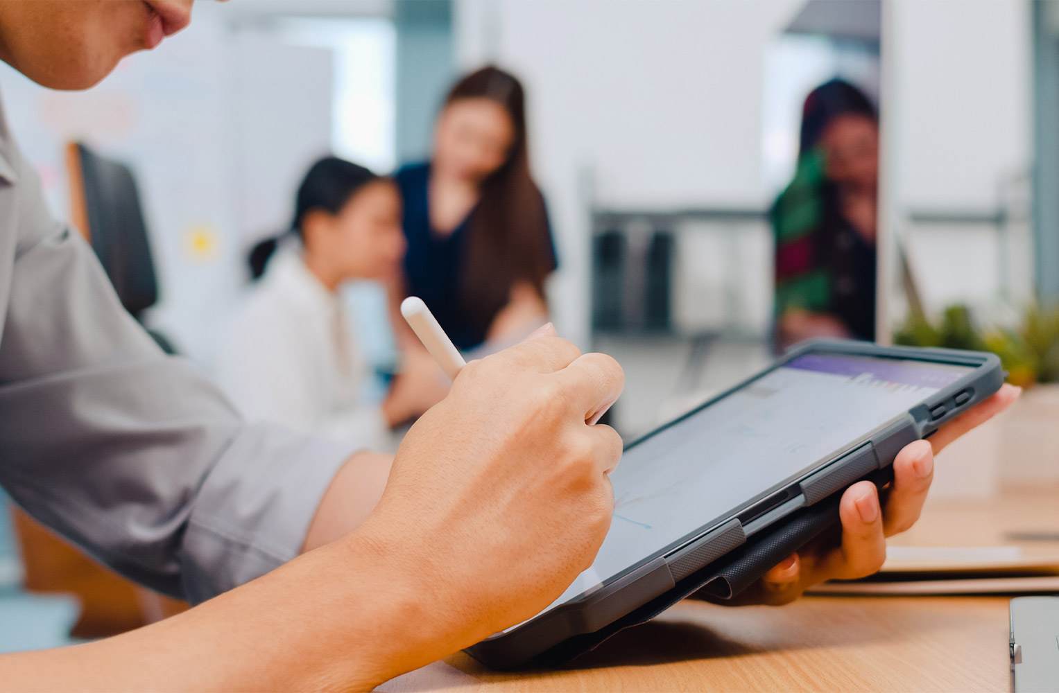 Persona utilizando un lápiz digital para firmar documentos en una tableta en un entorno de oficina moderna.