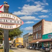 Cartel de bienvenida a Kissimmee, Florida, con la bandera del estado y el downtown histórico al fondo.