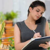 Inversionista extranjera tomando notas en cuaderno mientras habla por teléfono con asesor inmobiliario para dar el primer paso en bienes raíces en Florida