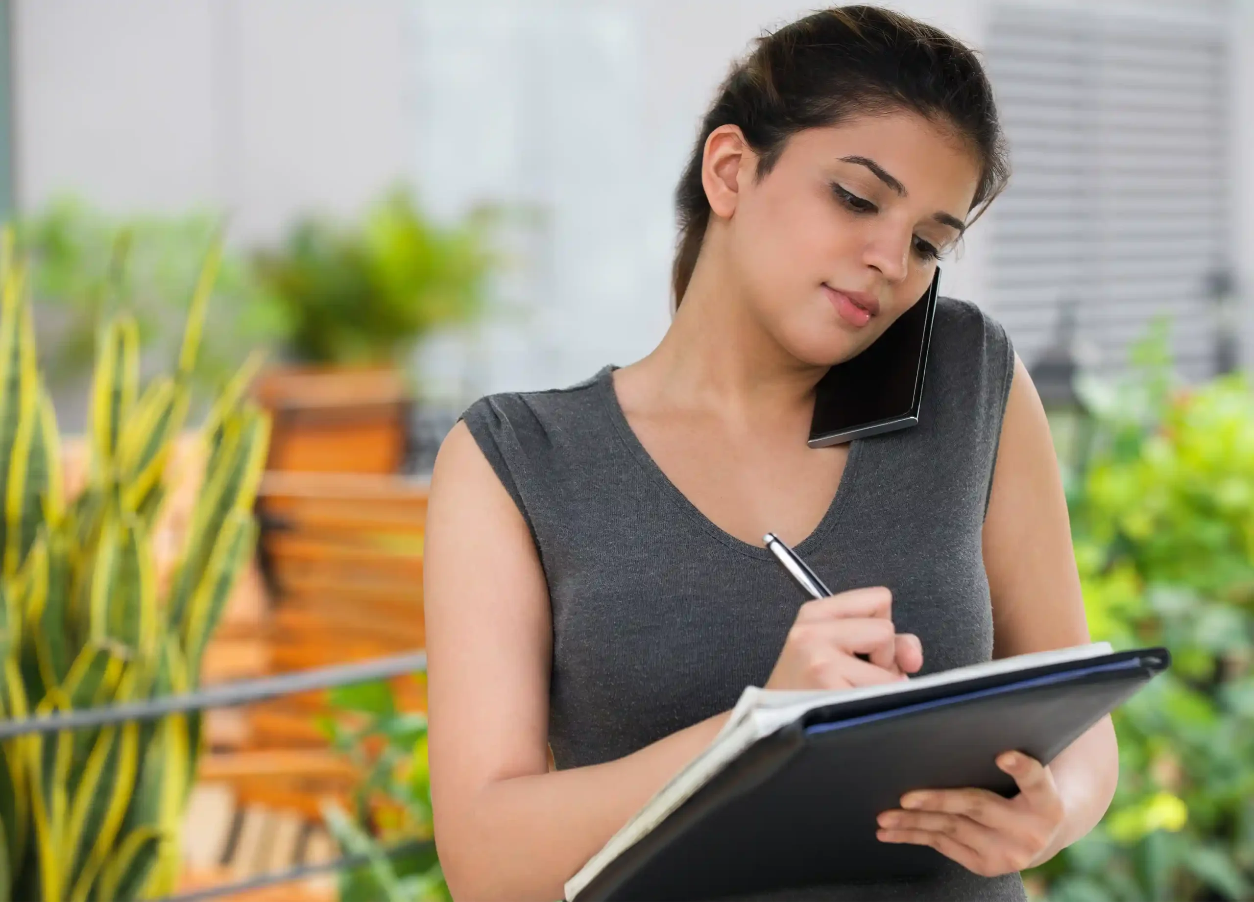Inversionista extranjera tomando notas en cuaderno mientras habla por teléfono con asesor inmobiliario para dar el primer paso en bienes raíces en Florida
