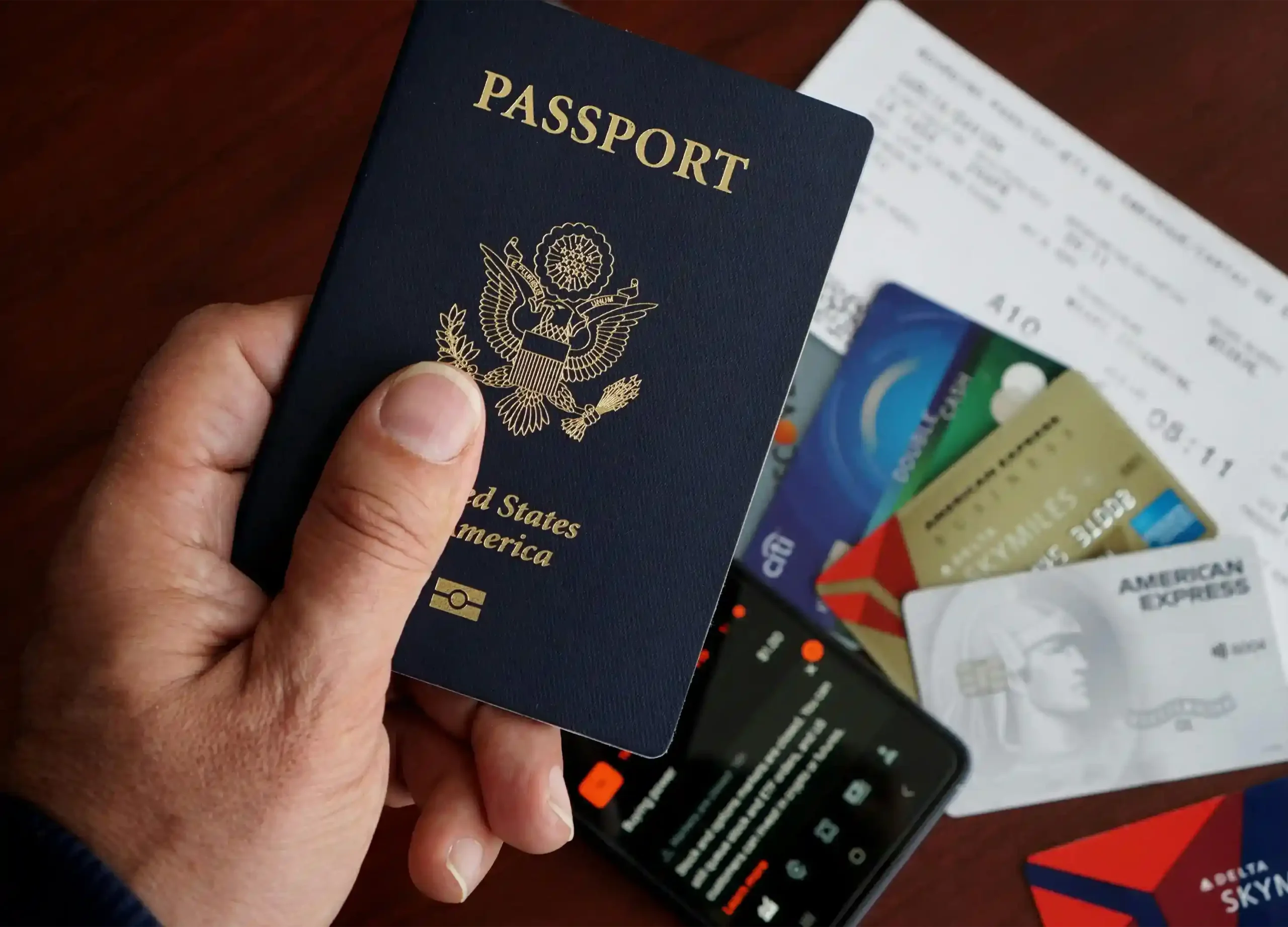 Mano sosteniendo pasaporte de Estados Unidos junto a tarjetas de crédito y documentos financieros, elementos clave para estructurar una inversión en bienes raíces en Florida con visa E-2