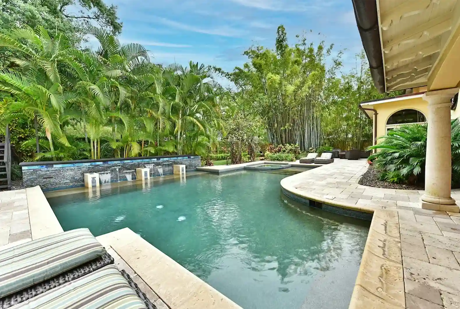 Piscina privada con cascada de piedra, jacuzzi y jardín tropical en propiedad vacacional de lujo en Orlando, Florida