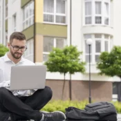Inversionista latinoamericano sentado frente a edificio residencial consultando propiedades en Florida desde su laptop