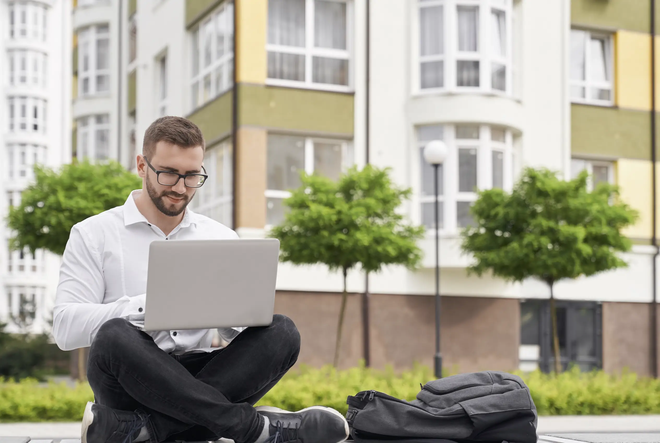 Inversionista latinoamericano sentado frente a edificio residencial consultando propiedades en Florida desde su laptop