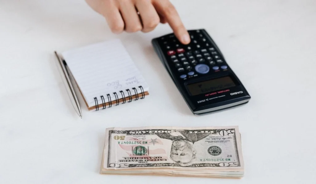 Hand using a calculator next to dollar bills to calculate Airbnb break-even point.