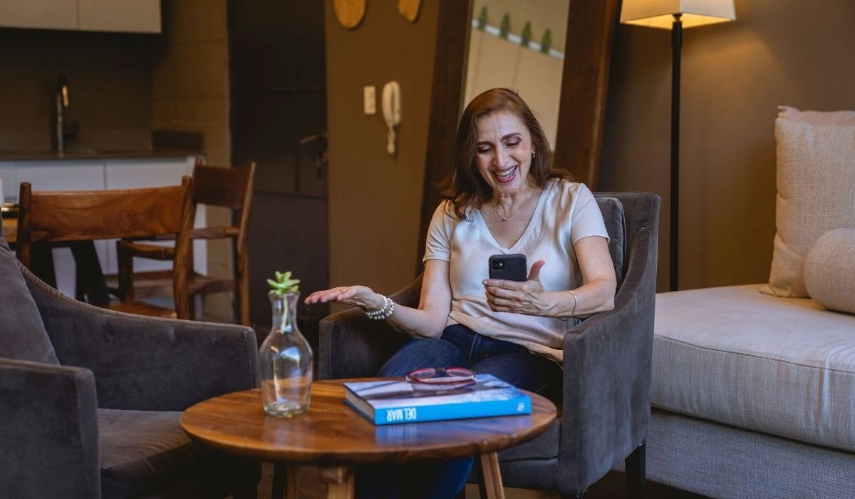 Mujer sonriente revisando su teléfono sentada en la sala de una renta vacacional en Orlando