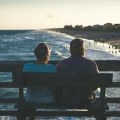 Pareja de adultos mayores sentada en una banca frente al mar durante el atardecer en una playa de Florida.